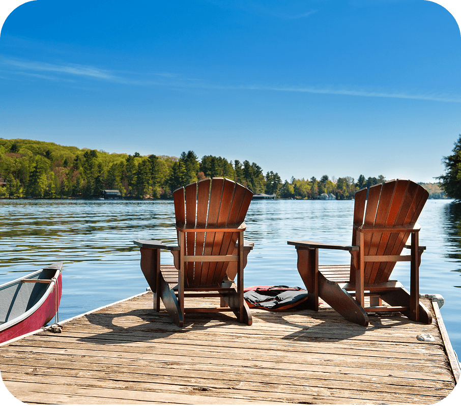 A lakeside dock, with a canoe and two chairs.